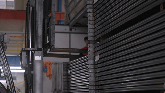 공장에서 금속 빔을 옮기는 지게차