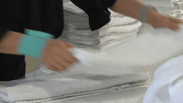 Worker folding multiple white towels in laundry factory
