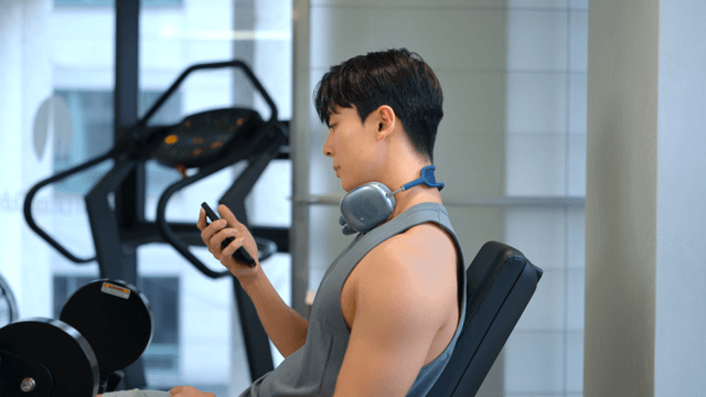Man using smartphone with headset around neck at gym