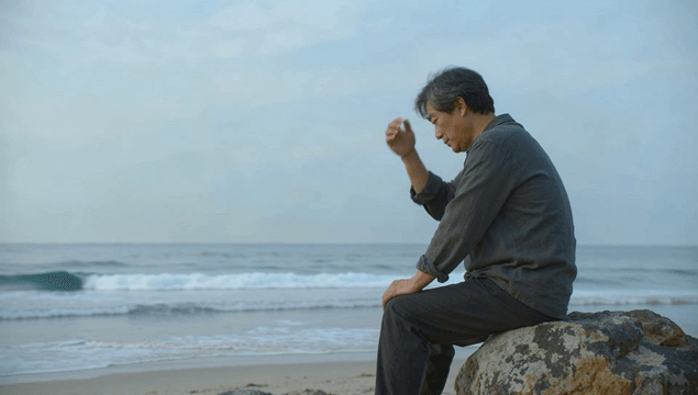 Elderly man deep in thought sitting on rocks by the beach
