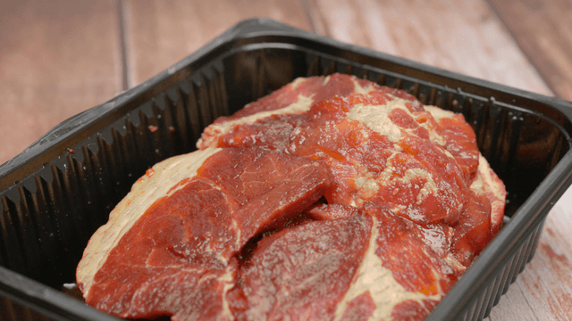 Fresh raw marinated pork in a black plastic tray