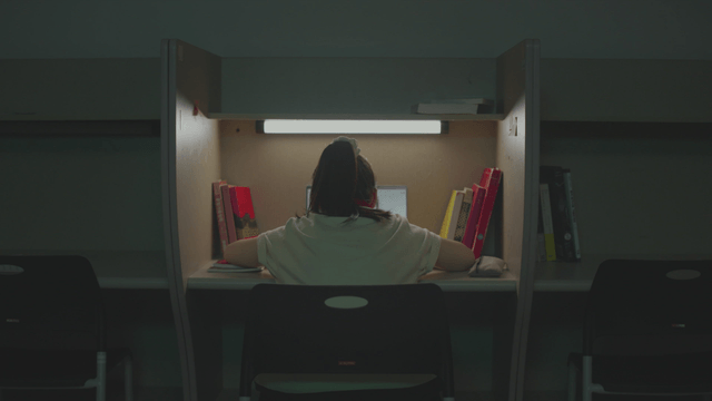 Back of a female student studying alone in a dark reading room