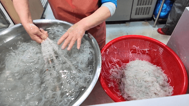 Bundles of ice fish lifted with chopsticks from water basin