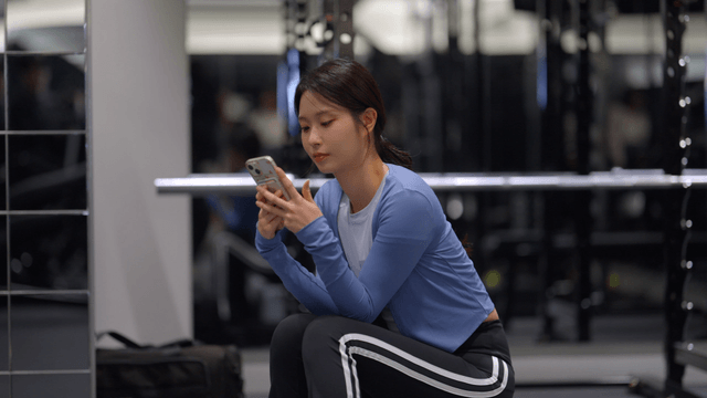 Young woman sitting in a gym using her phone