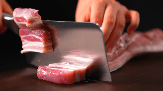 Slicing fresh pork belly on a wooden board