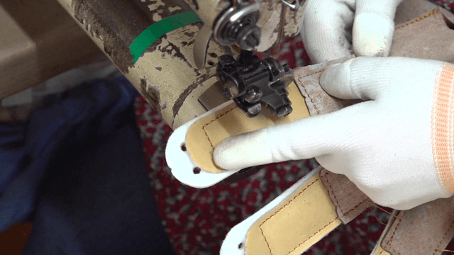 Gloved hands sewing leather pieces