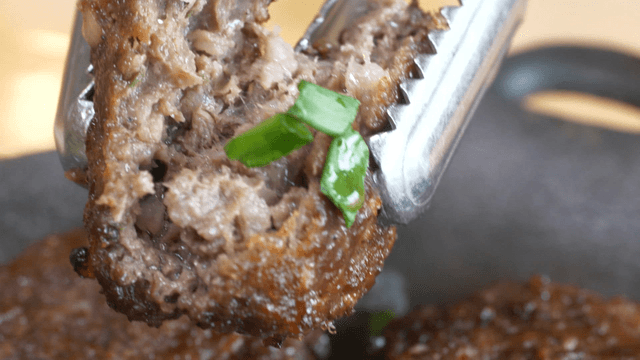 Grilled short rib patty being halved and garnished with green onion