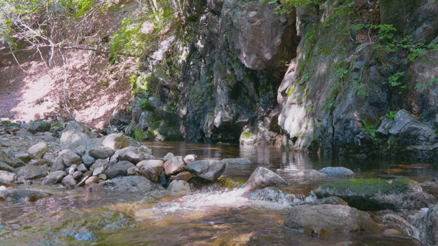 Calm stream flowing between rocks beneath a cliff