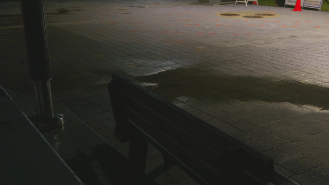 Rain falling on a night sidewalk with a bench