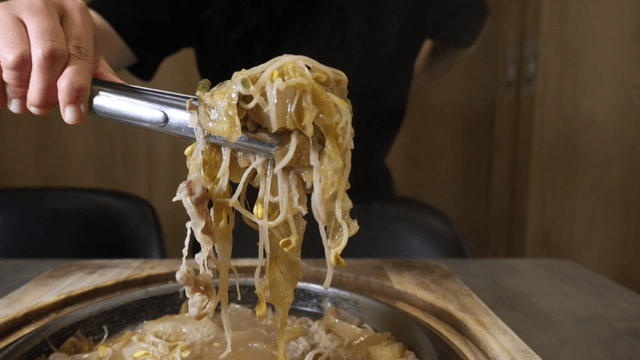 Tongs lifting beansprout white ripened kimchi stew