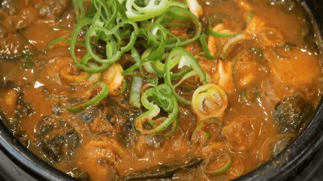 Boiling kimchi stew in hot earthen pot with green onion garnish