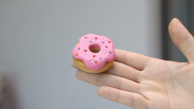 A hand holding a small pink donut made of clay
