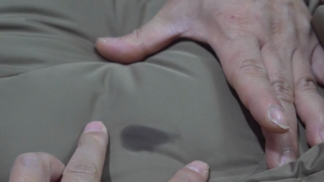 A finger pointing to an oil stain on clothes