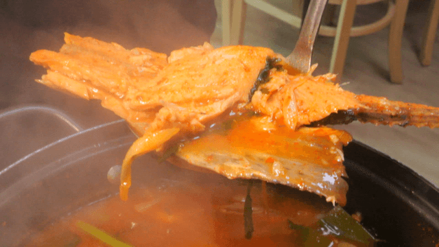 Ladle serving spicy trout stew from pot