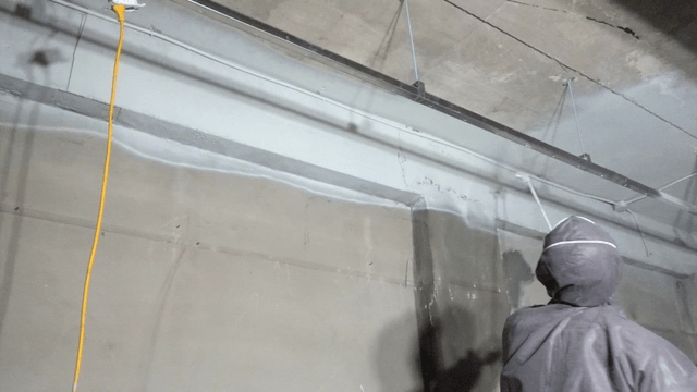 Worker painting ceiling with long spray gun