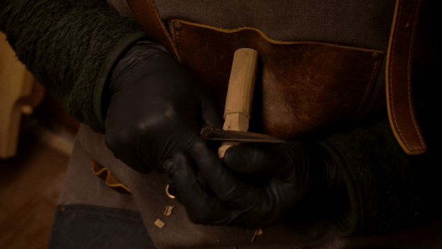 Artisan carving a wooden piece against his chest with a precise knife