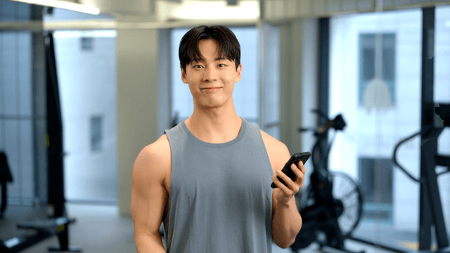 Man lifting dumbbells while holding smartphone at gym