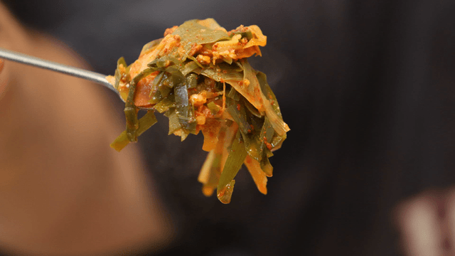 Spoon holding steaming budaejjigae with green onions
