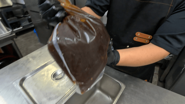 Chef shaking a plastic bag filled with dark broth