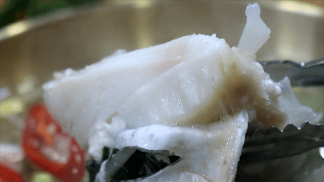 Tongs lifting thick cod fillet from soup