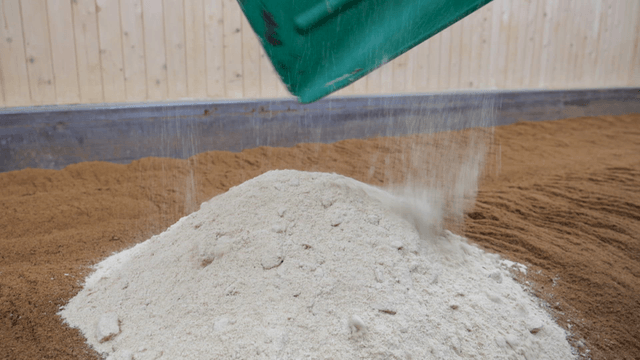 Wide shovel pouring white powder onto brown soil in warehouse