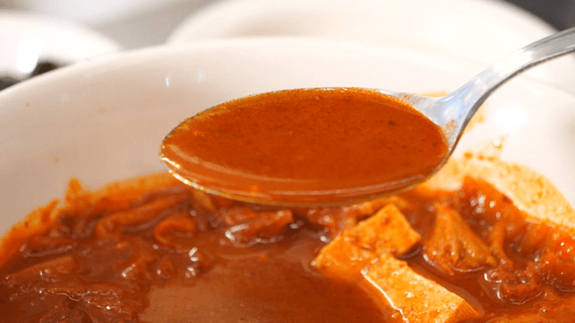 Rich kimchi stew broth scooped with spoon