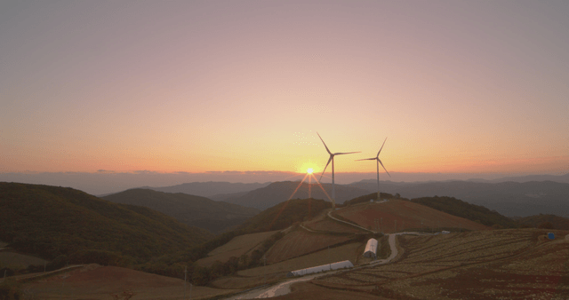 일출에 밭이 있는 언덕 위의 풍력 터빈