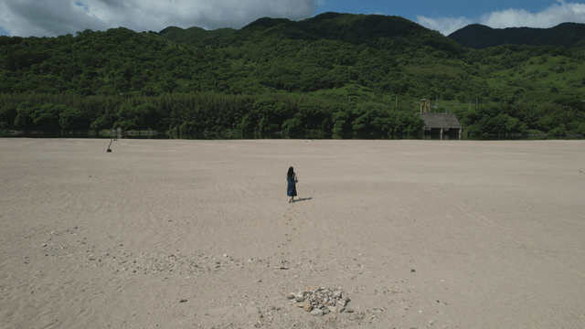 높은 산 아래 넓은 모래밭을 걷는 여성