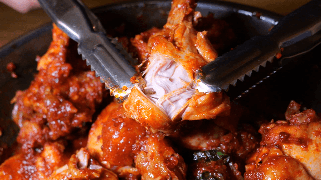 Tongs tearing spicy braised chicken drumsticks