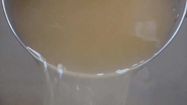 Clear rich broth pouring from a ladle