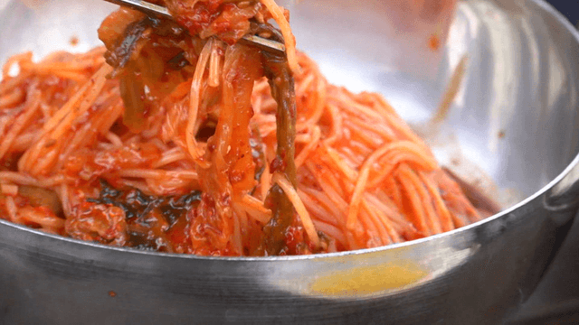 Chopsticks mixing spicy kimchi noodles in a bowl