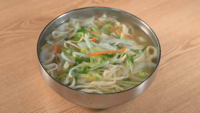 Hand-cut noodle soup with assorted vegetable garnishes on table