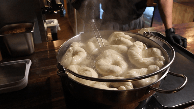 Baker taking boiled bagels out with skimmer