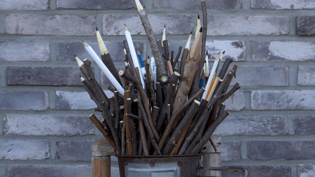 Wooden pencil sculpture with twig design against brick wall