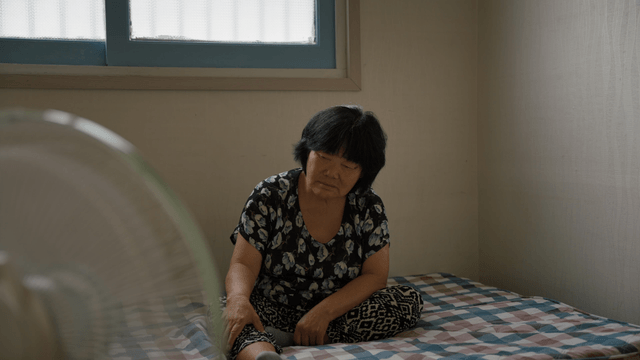 An elderly woman sitting on a bed indoors