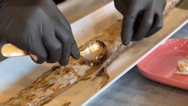 Gloved hands carefully removing bones from grilled cutlassfish