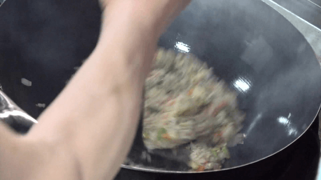 Fried rice being cooked with vegetables in a hot wok