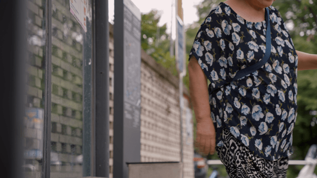 An elderly woman standing up from a bus stop bench