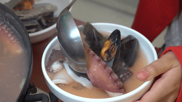 Ladle scooping chicken and seafood soup into a bowl