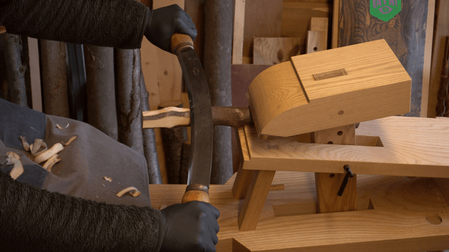 Woodcraft artisan shaping a wooden stick with a drawknife