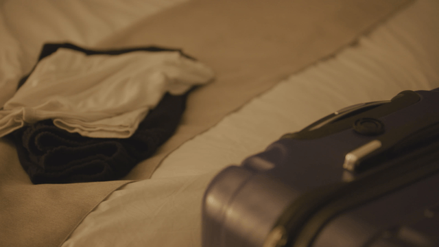 Suitcase on a bed with clothes nearby