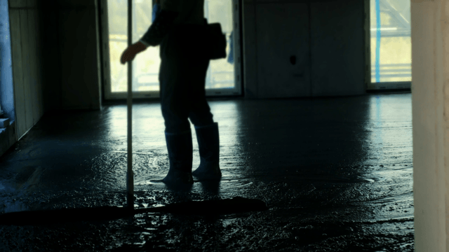 Worker smoothing concrete floor indoors