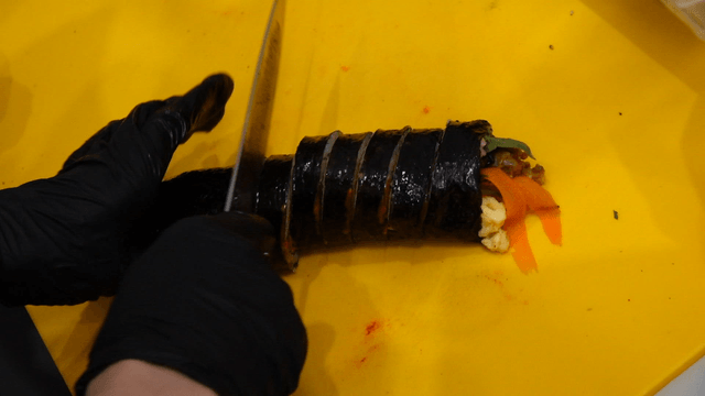Gimbap being sliced on a yellow cutting board