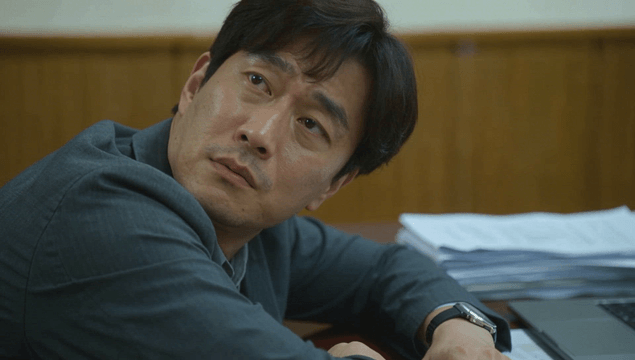 Office worker resting against desk with documents and laptop