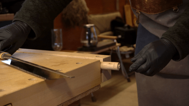 Craftsman cutting wooden piece with saw in workshop