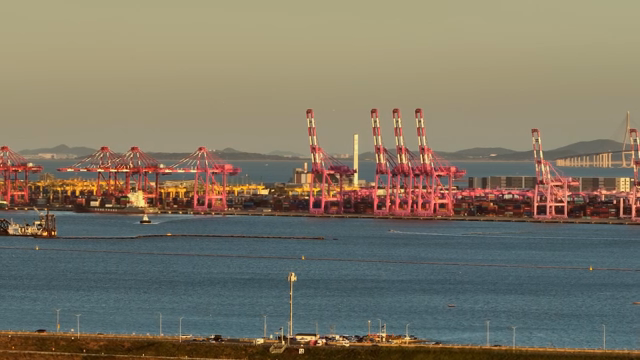 Cargo cranes at a busy port during sunset