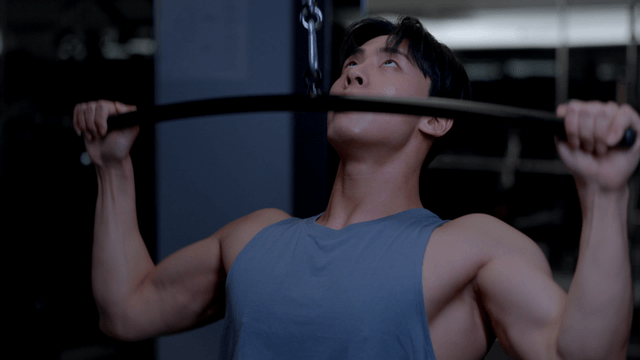 Young man training shoulders on lat pulldown machine