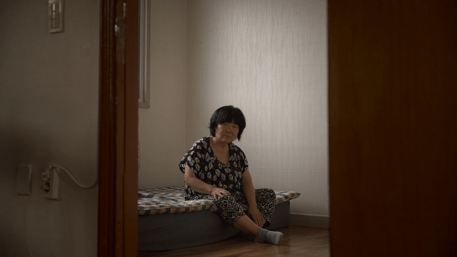 An elderly woman sitting on a bed indoors