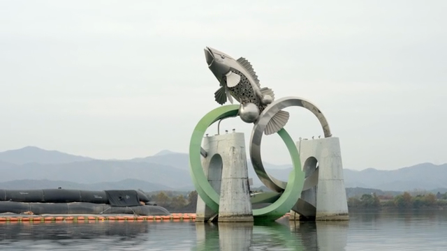 Large fish sculpture by a calm river
