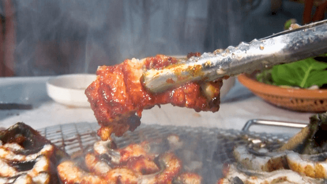 Tongs lifting grilled seasoned eels over charcoal fire
